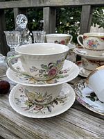 Close-up of tea cups and saucers with floral and bird motifs on a wooden surface