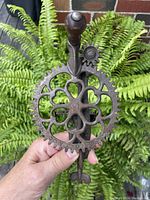 Front view of the antique iron apple peeler showing large decorative gear with four-leaf clover pattern and wooden handle.