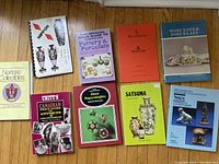 Photo showing the 9 reference books laid out on a wood floor, covering various antique and collectible topics such as Nippon porcelain, Canadian antiques, glass paperweights, Satsuma, and Worcester porcelain.