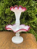 Full view of the two-tiered cranberry and milk glass epergne with ruffled edges and white glass pinched patterns at base and trumpet.