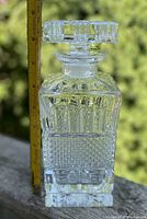 Front view of the clear glass Mid Century Modern Scotch decanter with geometric cut-glass pattern and stopper, shown next to a ruler for size reference.