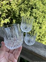 Four clear crystal lowball tumblers held and displayed outdoors, showing each tumbler's pattern and size.