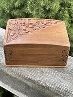Rectangular walnut box shown closed, with corner leaf carvings and smooth wood finish.