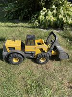 Side view of large yellow and black Tonka toy truck on grass, showing front loader bucket, wheels, and cab.