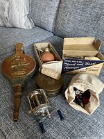 Overview photo of all items in the box lot displayed on a fabric surface showing the fishing reel, coloured bulb in box, brass box, bellow, medical device parts, and button bag.