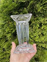 Photo of single crystal item held in hand showing square base with angular facets and overall transparent clarity, against a green background.