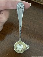 Photo of the Danish DFA sauce ladle showing the gold washed bowl and ornate handle held between fingers for scale.