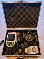 Metal carrying case open revealing laser level device, cables, and tripod mount laying inside foam padding.