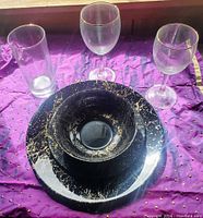 Set of black Arcoroc dinnerware with gold splatter design including plate, bowl, and three different styles of glasses (tall and two wine glasses) with gold rims.