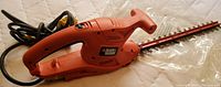 Photo showing entire orange electric hedge trimmer with cord and 16-inch blade on surface.