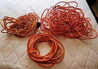 Three coiled orange electrical cords of varying lengths placed side by side.