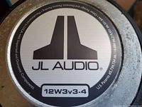 Close-up of the JL Audio logo and 12W3v3-4 model on silver metal center cap of the subwoofer.