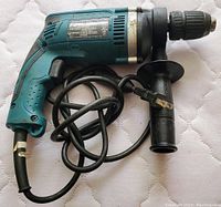 Photo showing teal Makita concrete hammer drill with black handle and power cord
