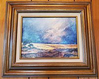 Framed painting showing a stormy plains landscape with a moody sky, rich color contrasts, and detailed brushwork.