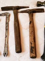 Photo showing two wooden-handled pickaxes with worn and rusty metal heads alongside a small hammer head.