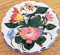 Close-up photo of a small floral side plate with colorful hand-painted flowers in underglaze on white ironstone ceramic, scalloped edge with blue trim.