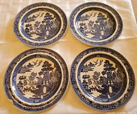 Four 10-inch Blue Willow patterned dinner plates laid out on table showing blue and white folk tale design.