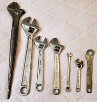 Seven wrenches in varying sizes including adjustable and fixed wrenches with visible wear and some rust.