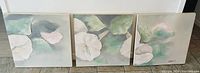 View of three connected oil paintings on canvas showing a continuous floral design in soft greens and whites.