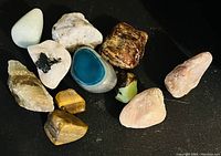 Nine assorted stones in varying colors including blue, white, pink, brown and yellow tones arranged on a black background.