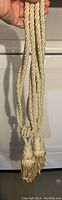 Full view of both cream-colored curtain tiebacks hanging, showing braided rope and tassels.