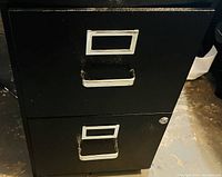 Photo of a two-drawer black metal filing cabinet with label holders and metal handles on each drawer. Lock on bottom drawer visible.