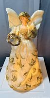 Photo of a lighted Christmas angel figurine wearing a white and gold decorative gown, holding a wreath and candle.