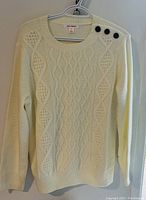 Front view of cream-colored knitted ladies sweater showing knit patterns and button shoulder detail