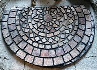 Half-round outdoor heavy rubber mat showing textured stone pattern in earth tones on concrete floor.