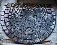 Photo of semi-circular outdoor heavy rubber mat with mosaic tile pattern showing wear and dirt.