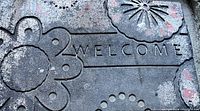 Close-up photo showing the textured rubber surface with floral patterns and the word 'WELCOME' embossed.