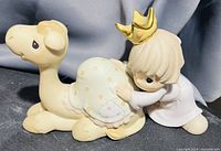 Image of a Precious Moments porcelain figurine showing a child wearing a gold crown hugging a camel figurine with decorative saddle.