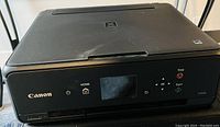 Black Canon TS5320 printer showing front control panel with LCD screen and buttons.