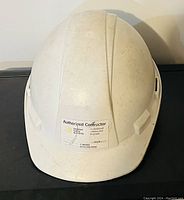 Front view of a white construction safety hard hat showing wear and a sticker indicating authorized contractor status.
