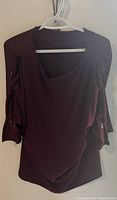Front view of burgundy blouse hanging on a hanger showing the square neckline and long sleeves.