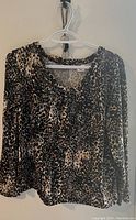 Full view of the leopard print blouse hanging on a white hanger against a beige wall.