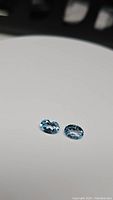 Two oval lagoon blue topaz gemstones on a neutral background showing facets and clarity.