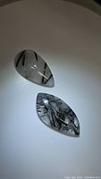 Two polished black rutilated quartz stones with black tourmaline inclusions on a white background, showing their glossy surfaces and natural inclusion patterns.