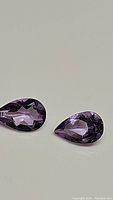 Pair of pear cut purple amethyst gemstones placed flat on light background showing facets and color.