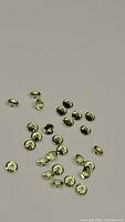 Top-down photo showing over 30 small round diamond cut apple green peridot gemstones scattered on a neutral background.