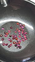 Multiple small round cabochon purple pink rhodolite garnet gemstones in metal container, showing size, shape, color and some inclusions