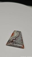 Photo showing polished trapezoidal Crazy Lace Agate gemstone highlighting its natural intricate pattern and color variation.