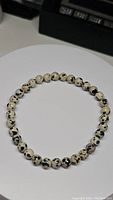 Natural dalmatian jasper bead bracelet arranged in a circle on a white round surface with black equipment slightly visible in background