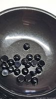 Photo of multiple round, 4mm diameter, cabochon cut jet black onyx gemstones in a black dish.