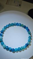 Front view of the blue agate beaded stretchy bracelet laid flat in a circle showing bead uniformity and color variation with a light background.