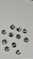 Photo showing 11 round cut natural green apatite gemstones, arranged on a neutral background to display clarity and color.