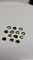 Photo of 13 polished pear-shaped green tourmaline gemstones in varying shades from light to dark green.