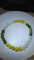 Top view of tri-colored jade bead stretchy bracelet laid flat in circular shape showing bead colors and pattern.