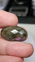 Close-up front view of natural labradorite gemstone showing checkerboard cabochon cut and some labradorescence with green and purple hues under light.