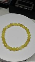 Top-down photo of a natural lemon jade bead stretchy bracelet laid out in a circle on a white plate, showing uniform round yellow beads.